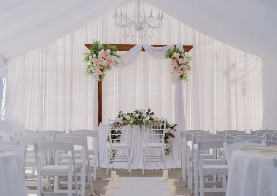 A wedding altar set with white drapery and florals, a chandelier above